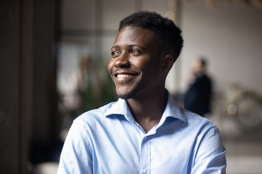 Happy African ethnicity businessman standing in modern workspace feels satisfied