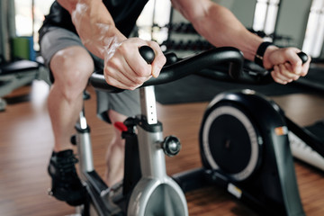 Fototapeta na wymiar Cropped image of sportsman riding stationary bike in gym before working out