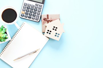 Business, finance , savings money, property loan or mortgage concept : Top view, flat lay of wood house model, gift box, blank notebook, calculator and coffee on table, ready for adding or mock up