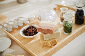 Stack of various soap bars on wooden tray with dried herbs and petals