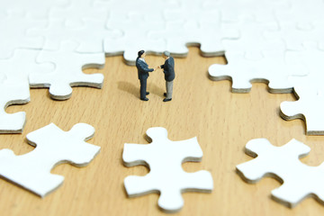 Business strategy conceptual photo - Miniature businessman make handshake partnership in the center of jigsaw puzzle piece 
