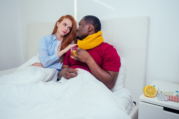 Obraz premium Young couple in knitted scarf in bedroom, sick and measure temperature