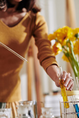 Woman using pipette when taking dye or essential oil from test-tube when making soap at home