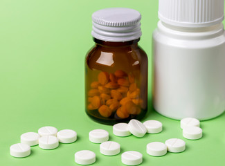 Two glass bottles of pills. Scattered white round tablets next to each other. Green flat background.