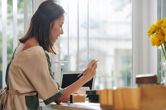 Pensive Female Small Business Owner Looking At Soap Bar In Her Hand And Thinking About Creative Name For The Product