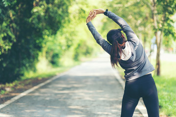 Healthy woman warming up before jogging run and relax stretching her arms and looking away in the road outdoor. Asian runner people workout fitness session, nature park background.