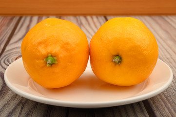 Two ripe yellow lemons on a white plate on a wooden background. Close up.