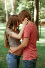 Fototapeta premium A happy married couple Husband hugs a beautiful adult pregnant wife. walks in a park. Second trimester. Holds his hands on her stomach. The benefits of walking during pregnancy, health care. Smiling