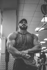 black and white photo of young strong active man with beard and big muscles posing in fitness gym