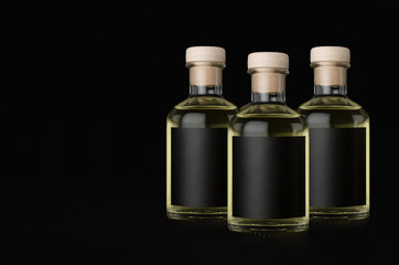 Three glass bottles for cosmetic, perfume, drink with black label, cork, yellow liquid on black background, mock up for design product, copy space.