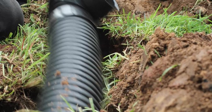 Worker digging out a trench to fit a new french drain pipe system in the ground