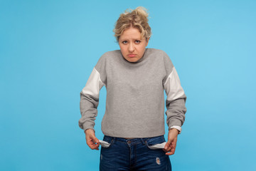 No cash. Upset poor woman with short curly hair in casual sweatshirt turning out empty pockets,...