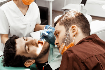 A young male dentist doctor treats a patient. Medical manipulations in dentistry, surgery. Professional uniform and equipment of a dentist. Healthcare Equipping a doctor’s workplace. Dentistry