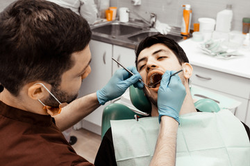 A young male dentist doctor treats a patient. Medical manipulations in dentistry, surgery. Professional uniform and equipment of a dentist. Healthcare Equipping a doctor’s workplace. Dentistry