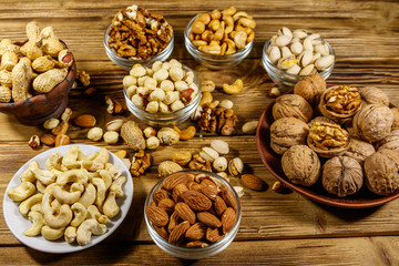 Assortment of nuts on wooden table. Almond, hazelnut, pistachio, peanut, walnut and cashew in small bowls. Healthy eating concept