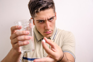 Young man with a glass of water and a pill in his hand