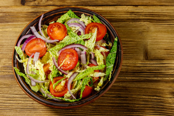 Healthy salad with savoy cabbage, cherry tomato, red onion and olive oil on wooden table. Top view