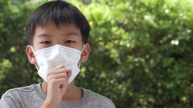 4k Young Asian boy wearing a face mask to protect virus and pollution has cough in a garden