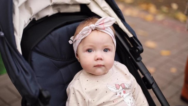 Close-up of adorable baby girl wearing a pink headband with a bow travelling in baby stroller on summer day outdoors.