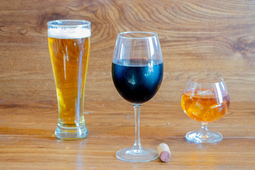 composition of alcoholic drinks with glass of whiskey, glass of clear beer and glass of red wine on stage of oak tables with a bottle cork