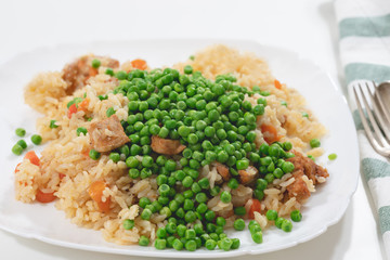 Rice with meat and vegetables close up on a plate on white background