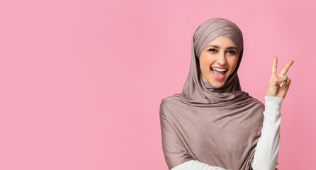 Positive arabic girl in hijab showing v-sign, demonstrating peace gesture