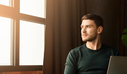 Entrepreneur Working On Laptop Looking Out Of Window In Workspace