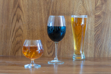 composition of alcoholic drinks with glass of whiskey, glass of clear beer and glass of red wine on stage of oak tables