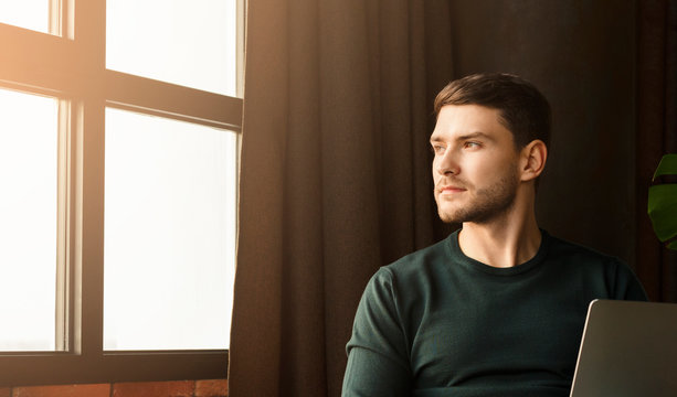 Entrepreneur Working On Laptop Looking Out Of Window In Workspace