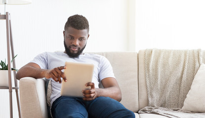 Concentrated african man reading news on digital tablet