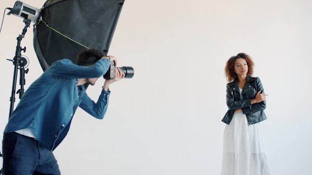 Slow motion of mixed race model beautiful young woman posing for camera in studio and male photographer taking photos with professional camera.