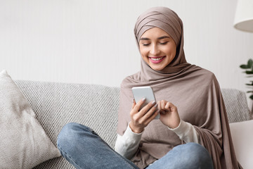 Happy arab woman scrolling social networks on smartphone at home