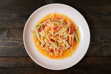 Papaya salad with chili and lemon in white dish on wooden table.(Som Tam Thai)