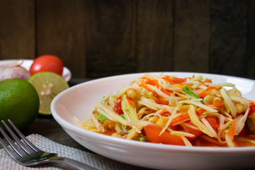 Papaya salad with chili and lemon in white dish on wooden table.(Som Tam Thai)