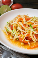 Papaya salad with chili and lemon in white dish on wooden table.(Som Tam Thai)