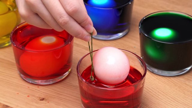 Young woman is dyeing easter eggs color at home kitchen table, design concept of preparing before egg hunting. 4K, close up shot.