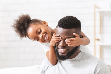Cute little black girl covering her dad eyes