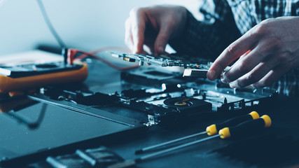 Electronics repair shop. Hardware maintenance. Male engineer working with laptop components. - obrazy, fototapety, plakaty
