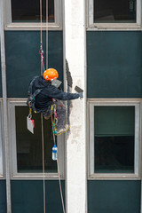 trabajador vertical colgado de una cuerda reparando una fachada ó obrero vertical reparando un...