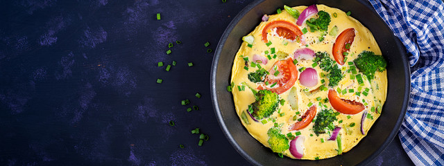 Omelette with broccoli,  tomatoes and red onions in iron skillet. Italian frittata with vegetables. Top view, banner
