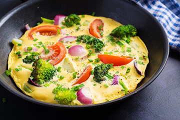 Omelette with broccoli,  tomatoes and red onions in iron skillet. Italian frittata with vegetables.