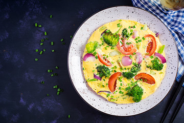 Omelette with broccoli,  tomatoes and red onions on dark table. Italian frittata with vegetables. Top view, overhead