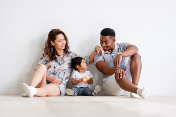 Young loving family asian mom african-american dad and mixed race daughter sit on floor at home resting at weekend. Concept of happy young loving and caring family. Understanding Parents and Children