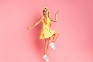 Cheerful woman dancing jumping over pink studio wall