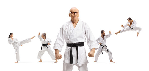 Elderly karate master with black belt posing with people exercising behind