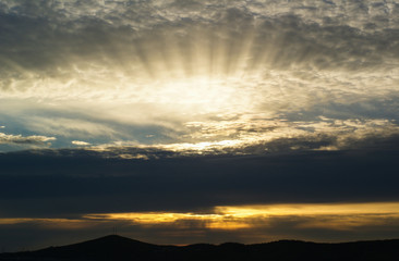 The rays of the setting sun behind the clouds.