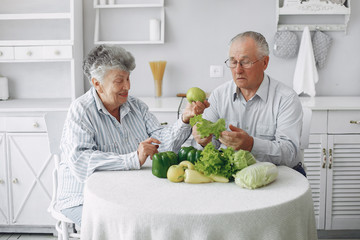 Couple in a kitchen. Grandparents sitting at home. Woman with vegetables