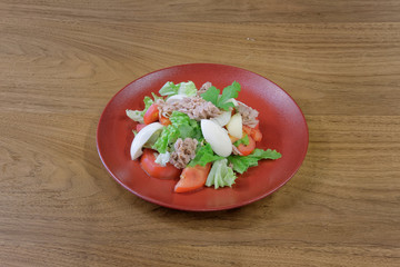 Restaurant food served on a red plate. Fish, cheese, salad, vegetables, sauce.