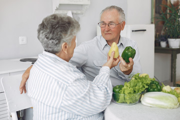 Couple in a kitchen. Grandparents sitting at home. Woman with vegetables