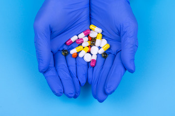 Different pills in hand in a medical glove on a blue background. Medicine. Treatment.